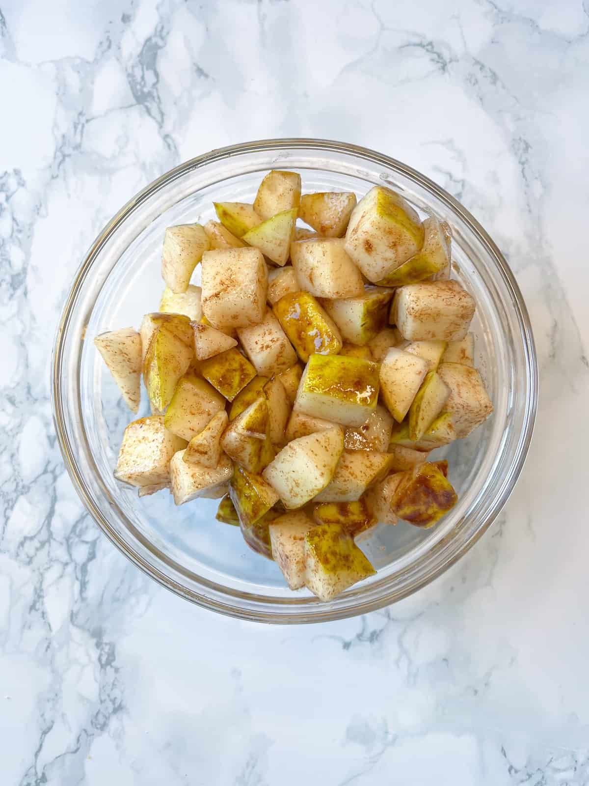 diced apples mixed with pure maple syrup, ground cinnamon, and avocado oil in a glass bowl