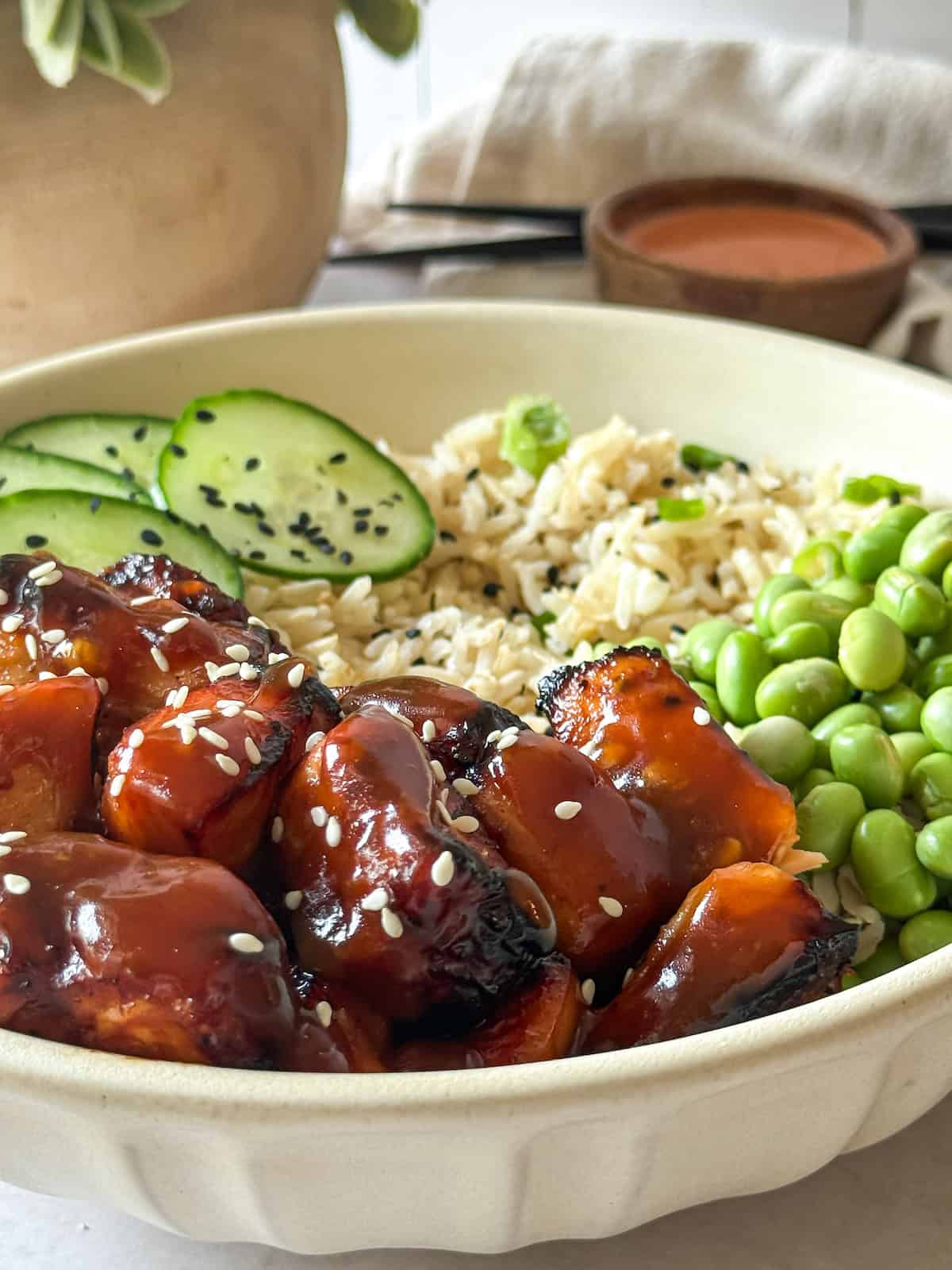 Honey garlic salmon bites in a bowl with edamame, brown rice, and cucumber.
