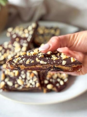 human hand holding a date snickers with more date snickers on a plate in the background.