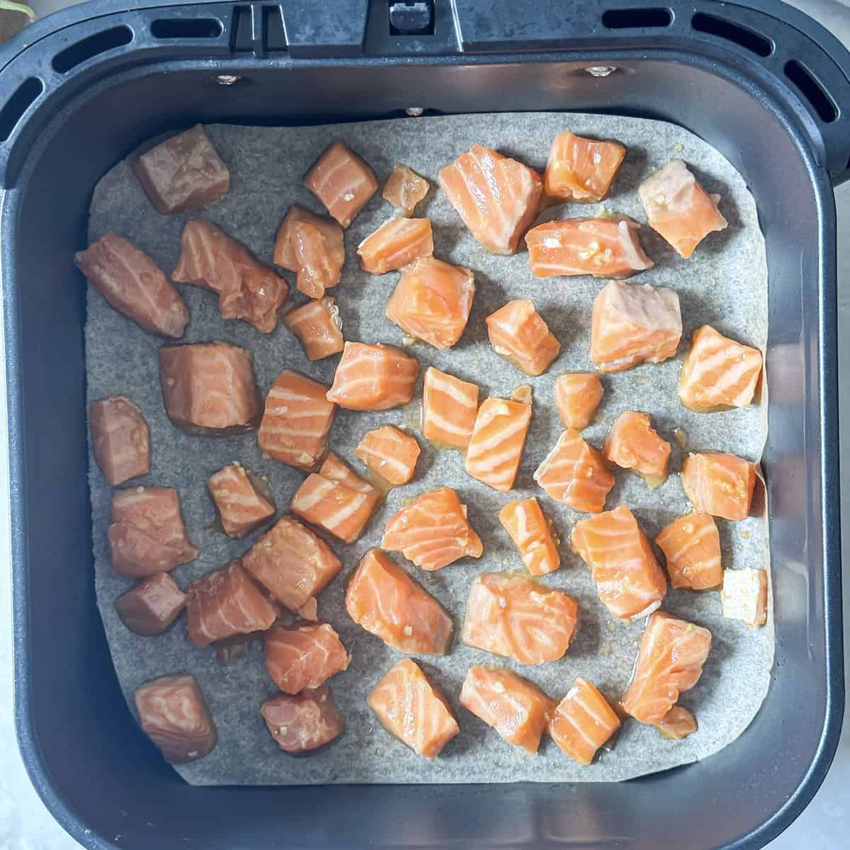 overhead view of salmon bites in an air fryer before being cooked.