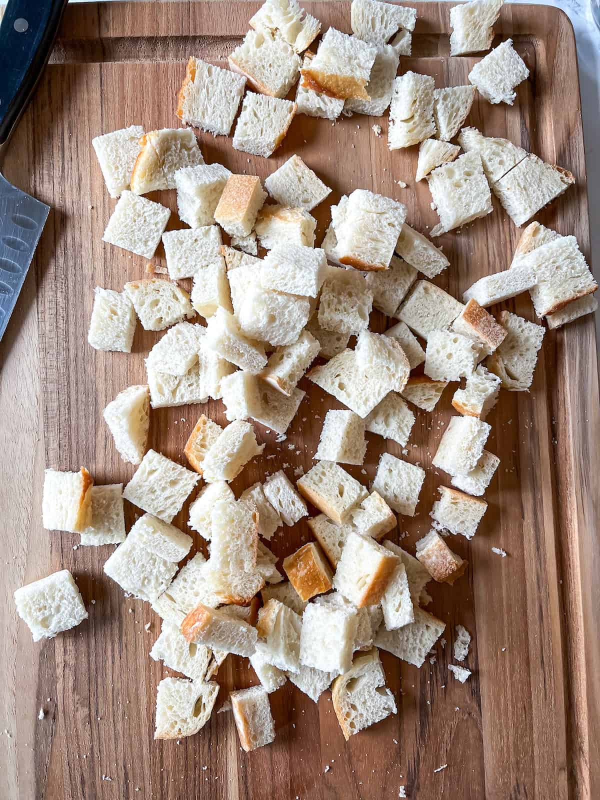 sourdough bread cubes on a wooden cutting board with a knife in the background