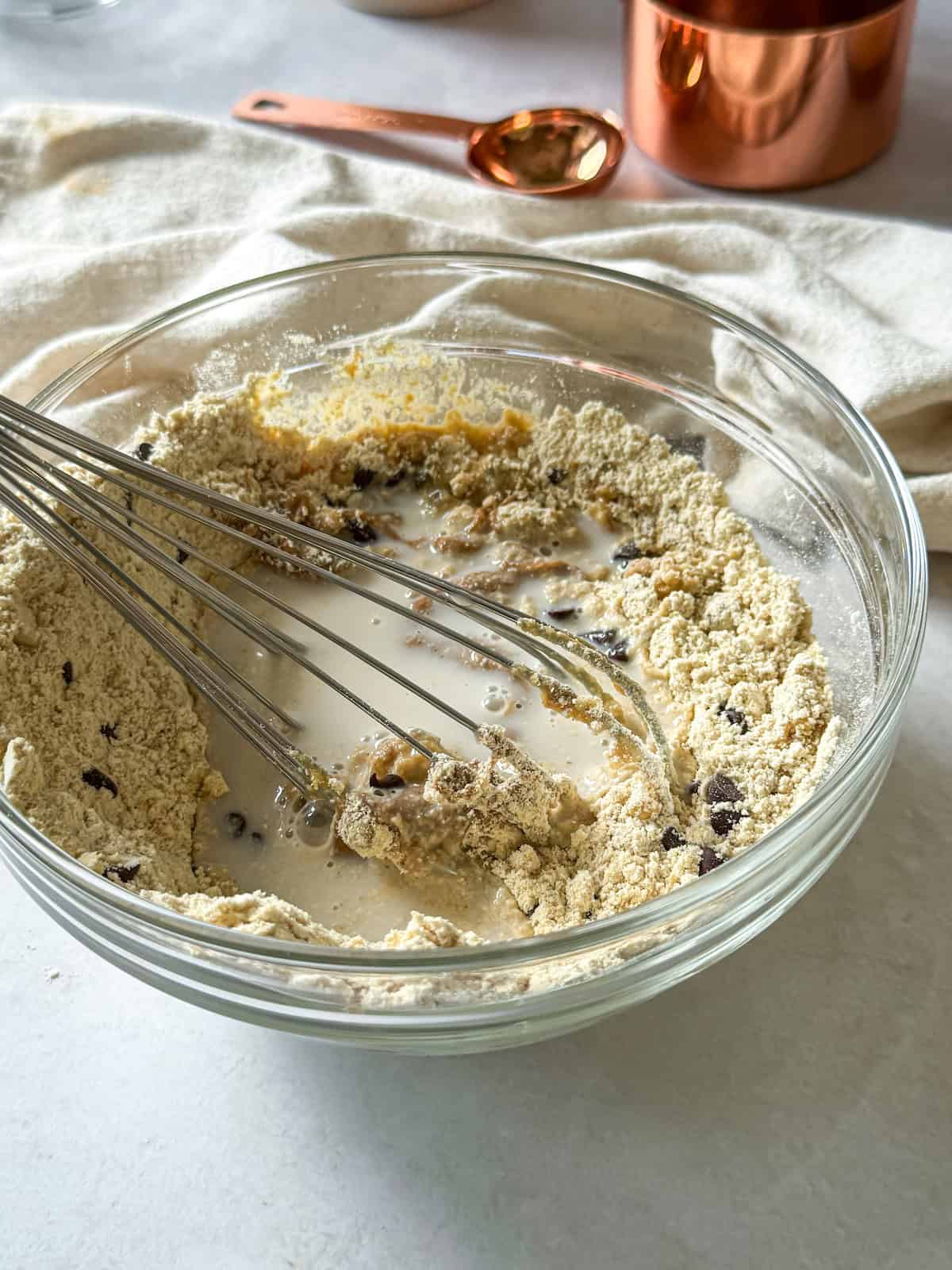 The wet ingredients added to a glass bowl with dry ingredients for protein cookie dough balls.