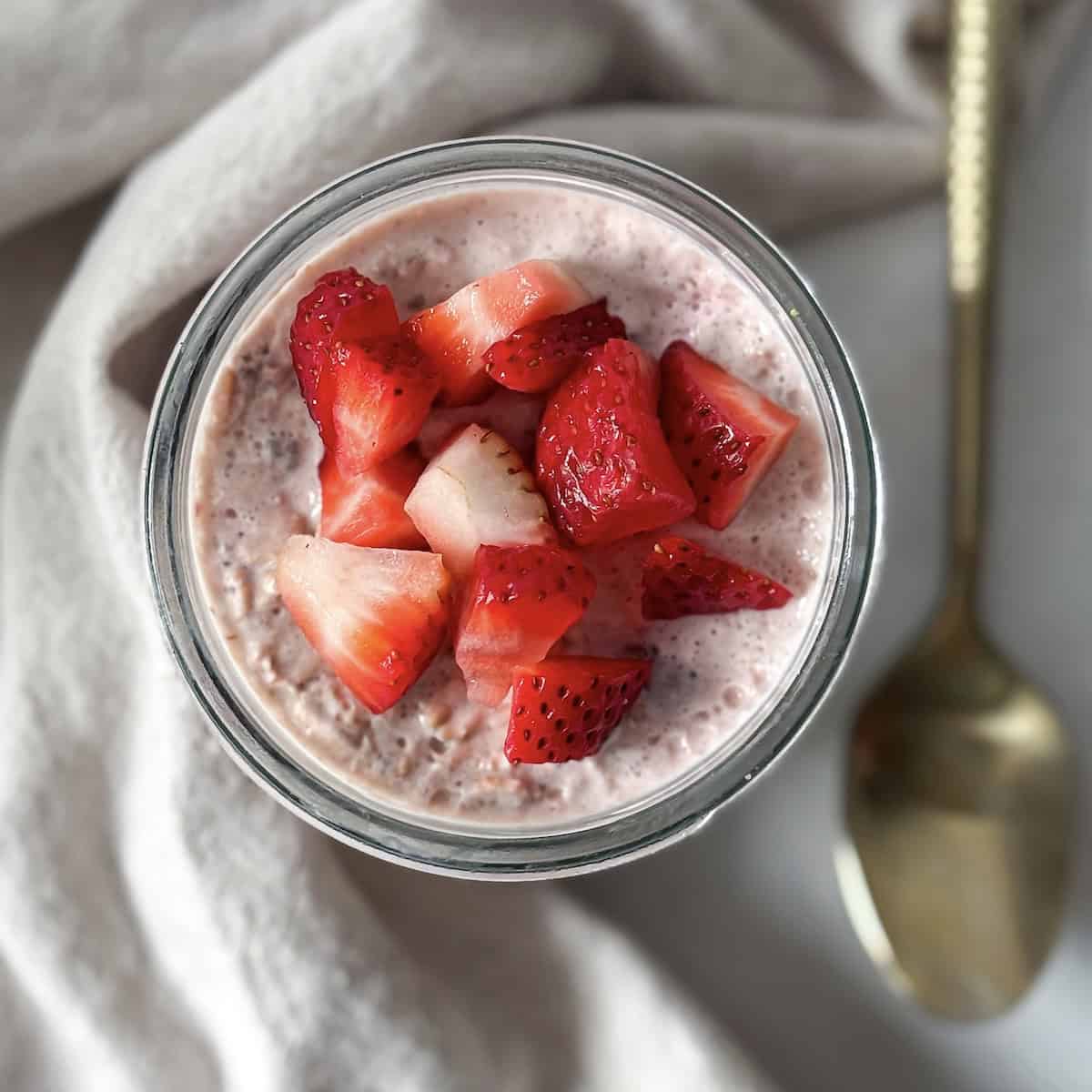 overhead view of strawberries and cream overnight oats in a mason jar with a spoon.