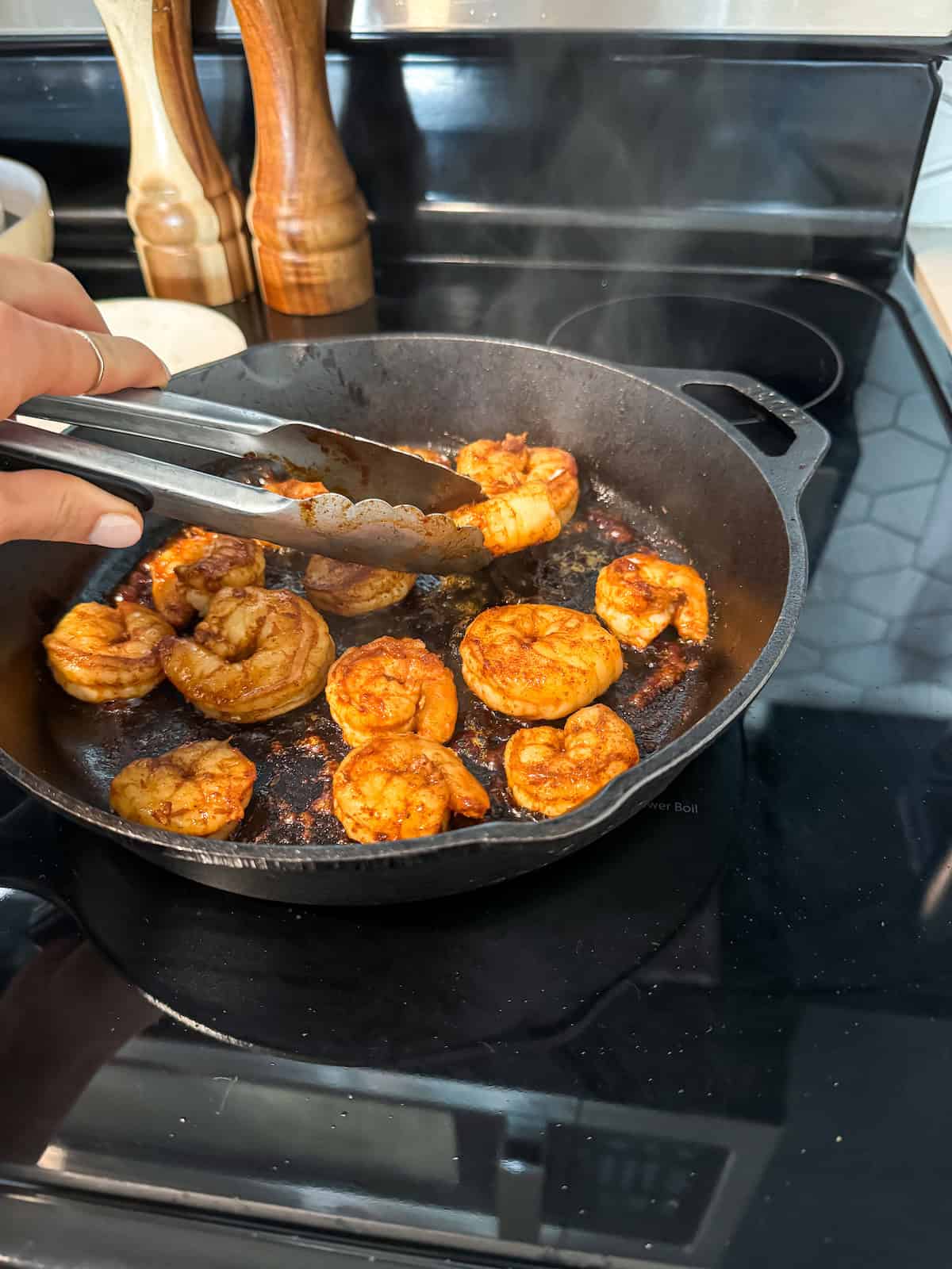 A hand flipping shrimp in a cast iron skillet.