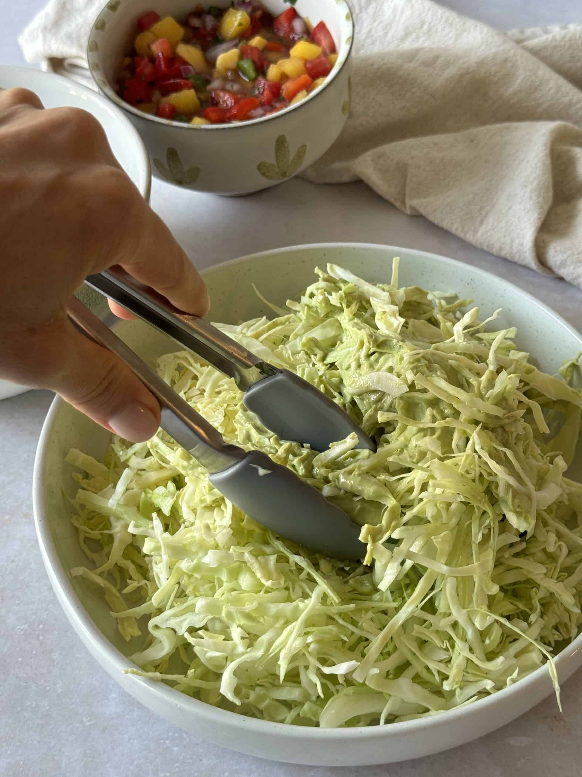 a hand mixing cabbage with avocado lime crema.