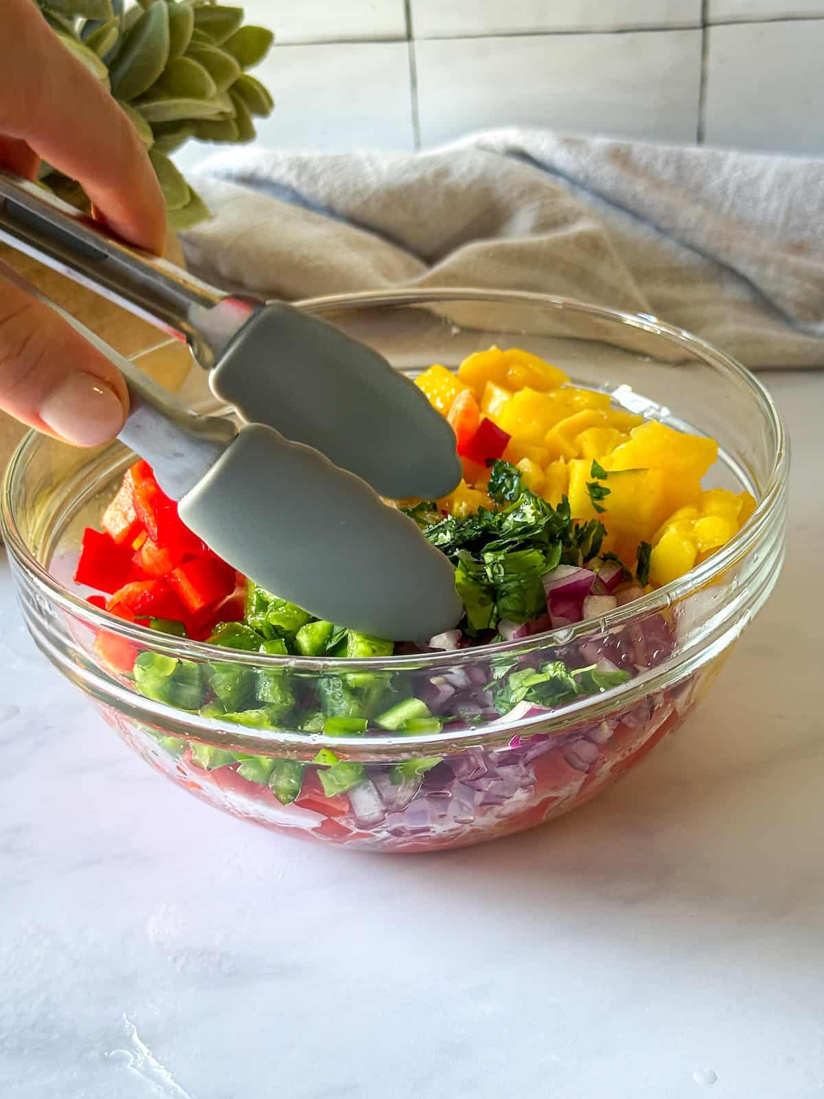 A hand mixing mango pico de gallo.