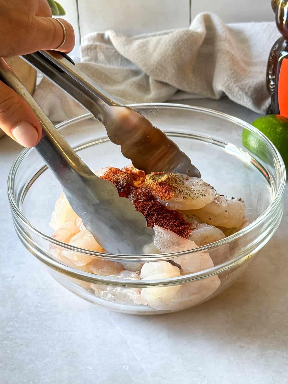 A hand mixing shrimp with spices and honey and lime.