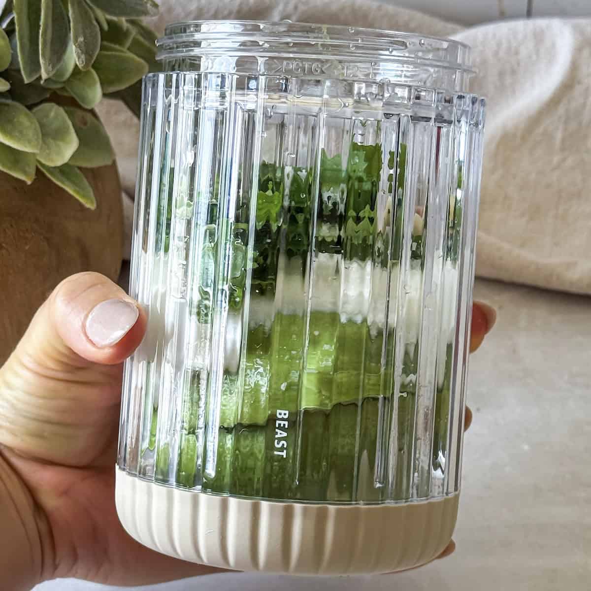 human hand holding a blender with avocado lime crema ingredients.