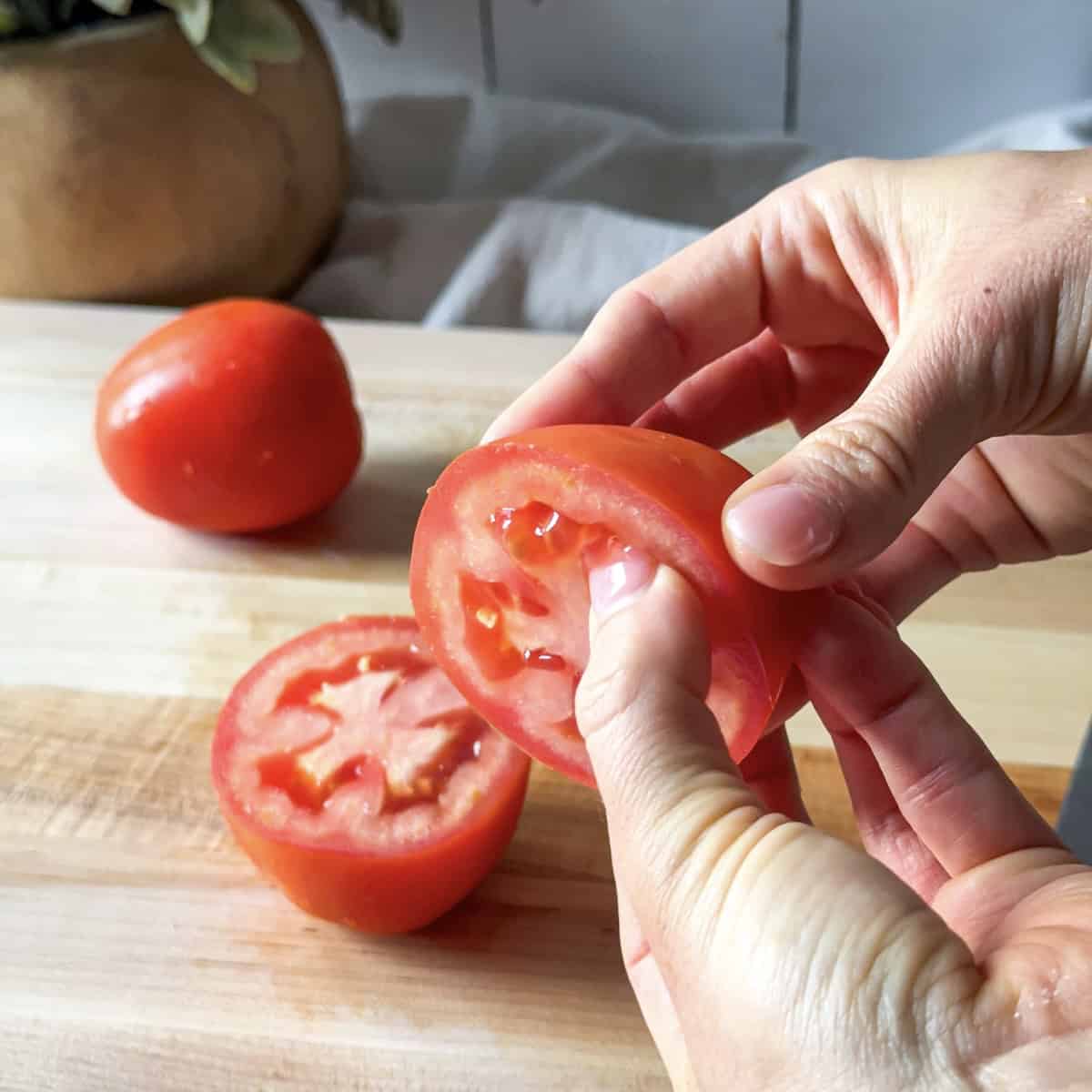 human hand removing seeds from a roma tomato.
