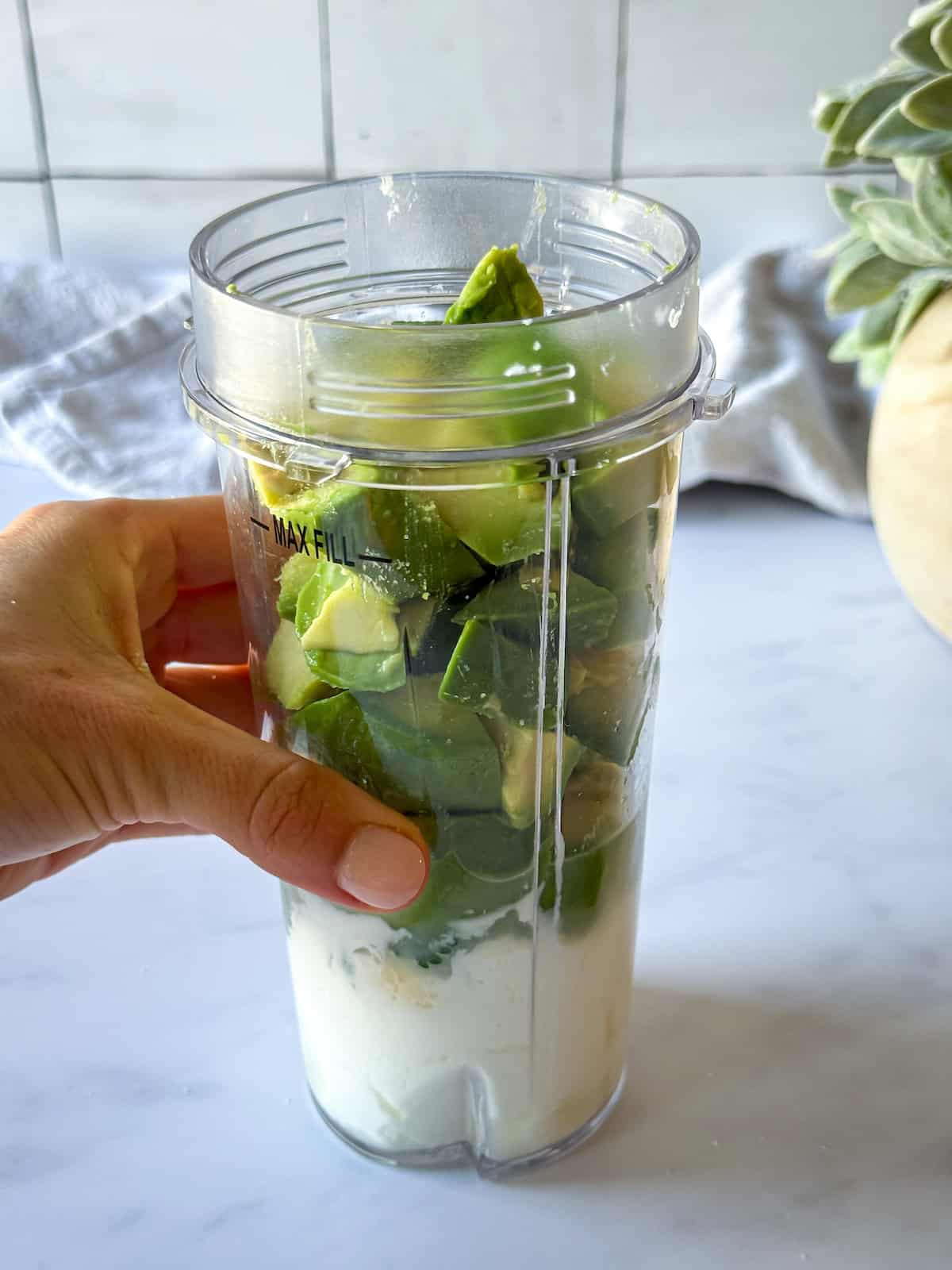 A hand holding a blender with avocado crema ingredients in it.