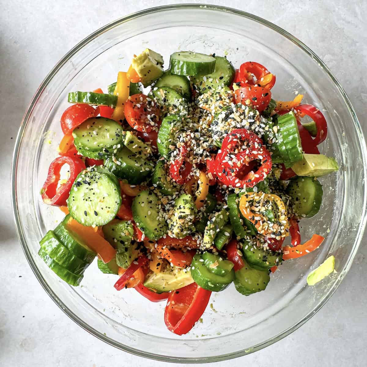 overhead view of cucumber pepper salad ingredients in a glass bowl.