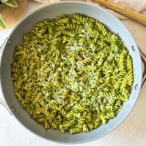 overhead view of green pasta sauce in pasta in a skillet with parmesan on top.
