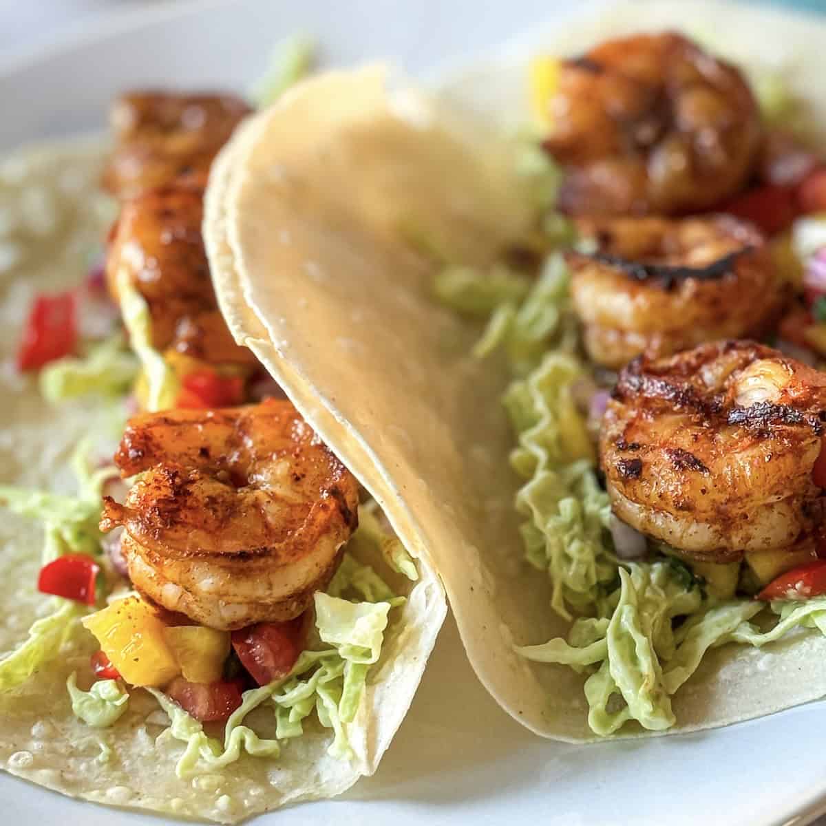 2 shrimp tacos with avocado crema slaw, mango pico de gallo, and spicy shrimp in a tortilla on a plate.