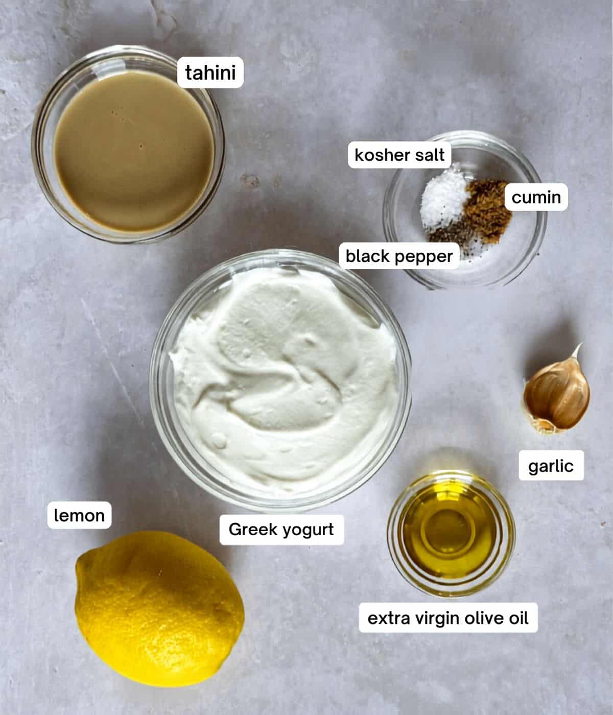 ingredients for yogurt tahini sauce in separate bowls on a grayish white background.