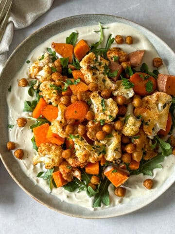 Nourish bowl with sweet potatoes, chickpeas, arugula, cauliflower, carrots, and yogurt tahini sauce.