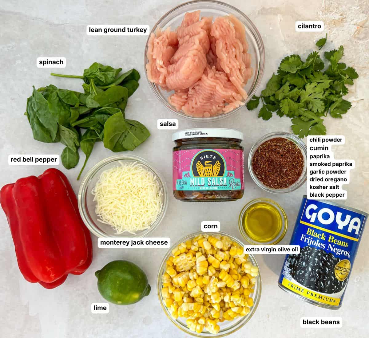 Ingredients for turkey taco skillet in separate containers labeled on a tannish white background.