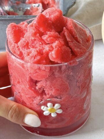 a human hand holding a cup with a white flower on it with Watermelon Strawberry Sorbet in it.