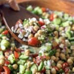 A human hand scooping chickpea cucumber salad.