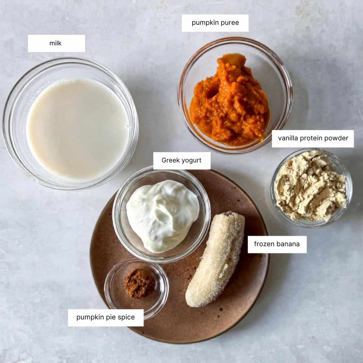 ingredients for pumpkin protein smoothe in individual bowls or plates on a grayish white background.