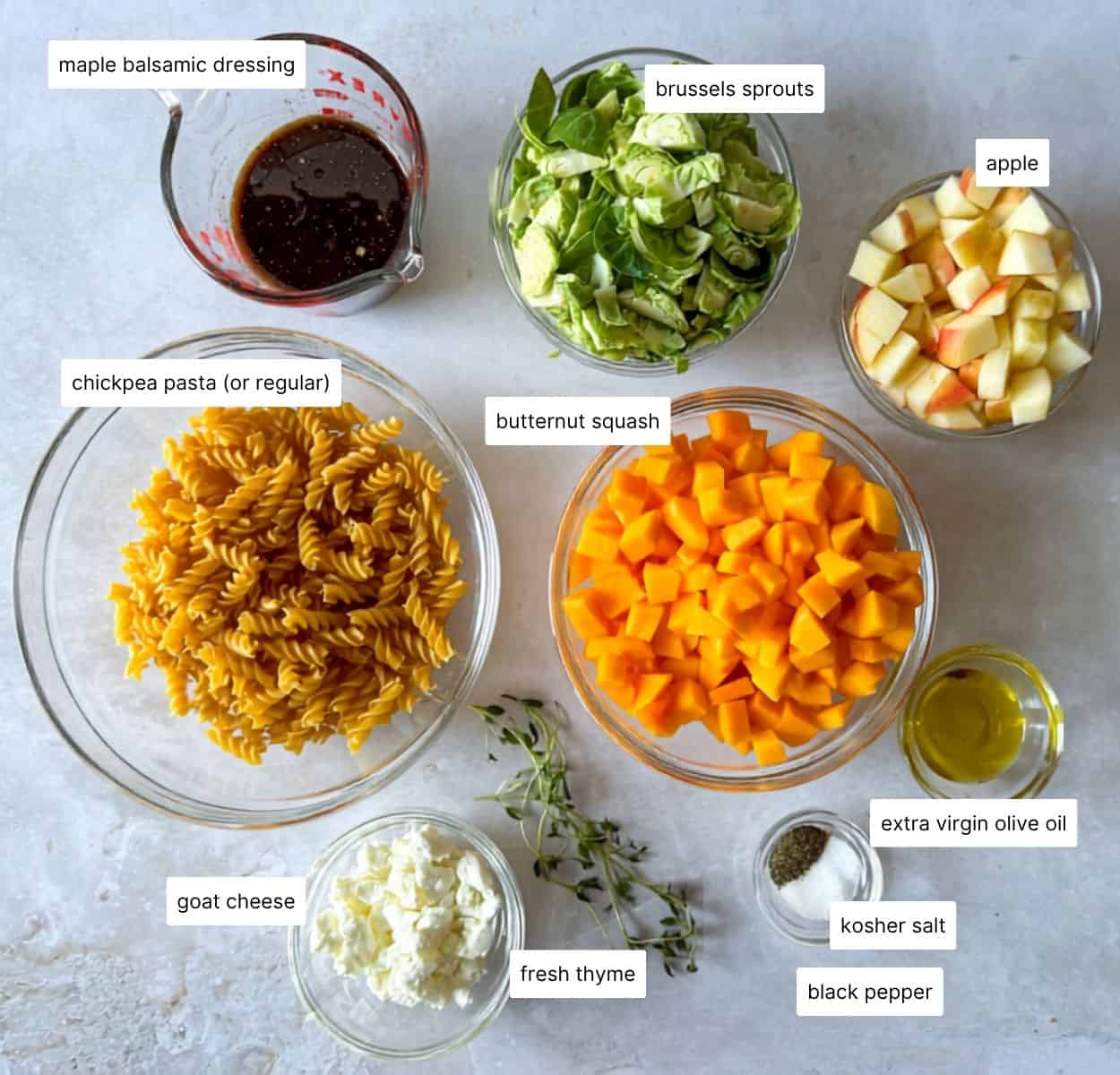Ingredients for fall pasta salad in individual containers on a white gray background.