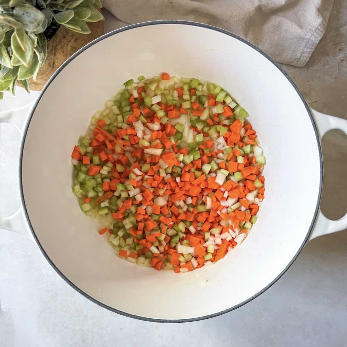 Finely diced carrots, celery, and onion in a large white Dutch oven.
