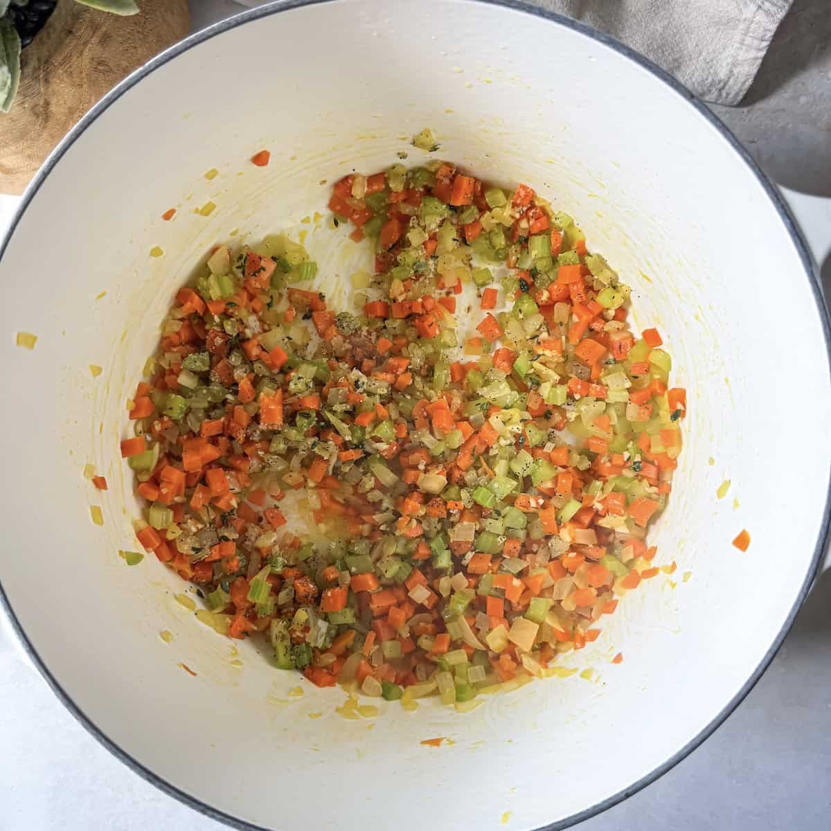 Sauteed carrots, celery, and yellow onion in a white Dutch oven with garlic, fresh thyme, kosher salt, and pepper added to it.