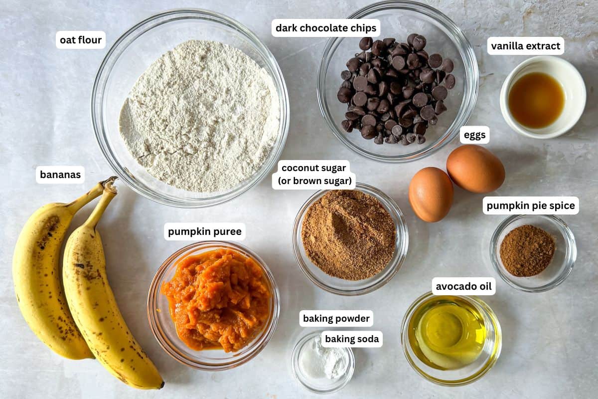 Ingredients for pumpkin banana bread muffins in separate containers on a table with a tanish white background.