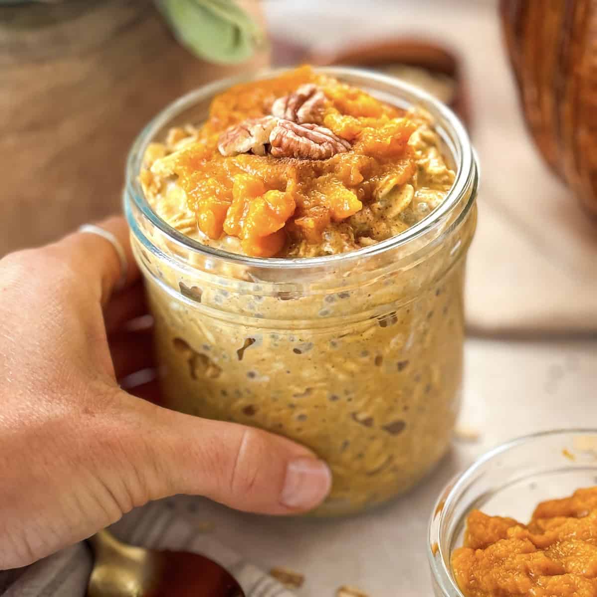a human hand holding onto a mason jar with pumpkin pie overnight oats. 