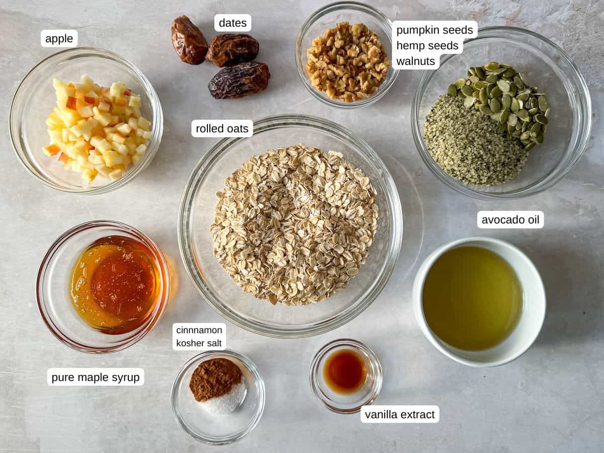 Ingredients for Apple Pie Granola in separate containers on a table with a grayish white background labeled.