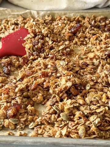 Apple pie granola on a baking sheet with a red spatula in the background.