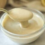 Maple Tahini Dressing in a bowl with a spoon holding some up to show how thick and creamy it is.