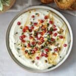 Whipped Ricotta dip with honey on a plate with pomegranate and honey on top overhead view.