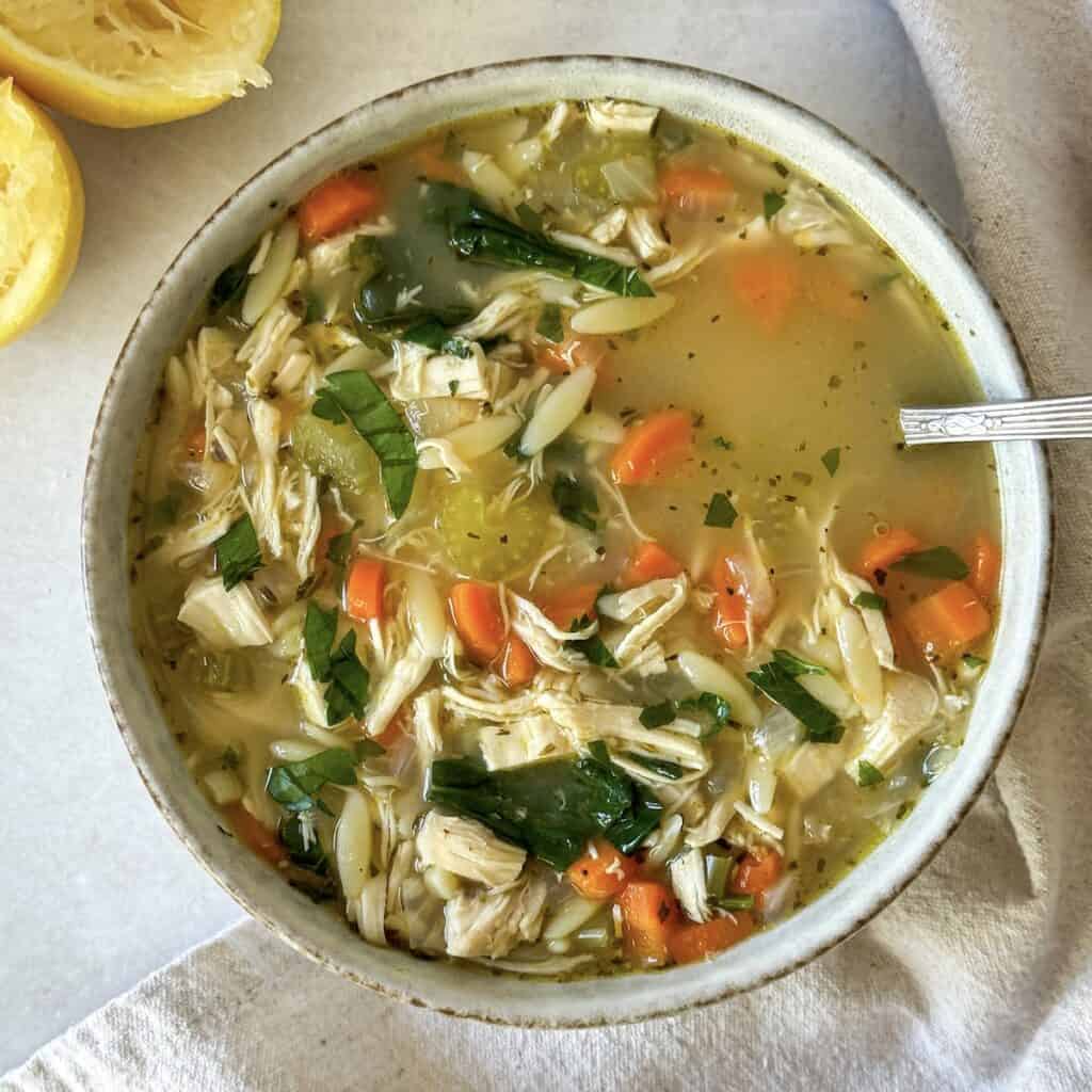 bowl of lemon chicken orzo soup overhead view with lemon in the background