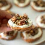 sweet potato with ricotta and pecan & date topping with thyme. A human hand is holding one up.