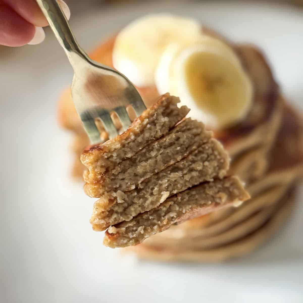 a human hand holding a fork with a bite of banana pancakes