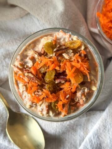 overhead view of carrot cake overnight oats with grated carrots and golden raisins on top and a spoon next to it.