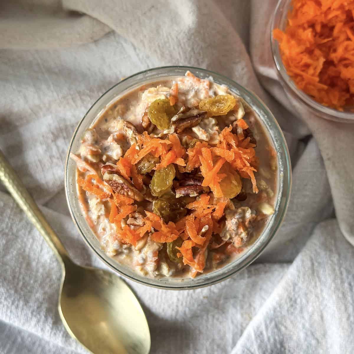 overhead view of carrot cake overnight oats with grated carrots and golden raisins on top and a spoon next to it.