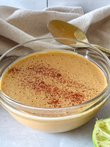 southwest salad dressing in a glass bowl with limes behind it. and a spoon.