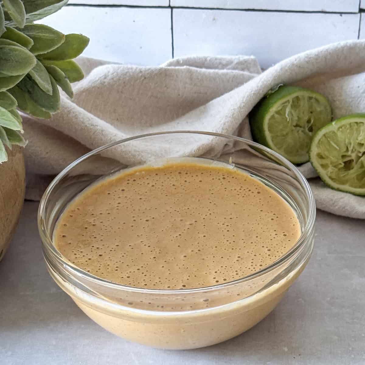 southwest salad dressing in a glass bowl with limes behind it.