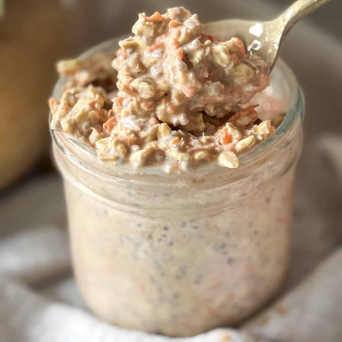 spoon pulling a bite of carrot cake overnight oats with grated carrots and golden raisins on top.