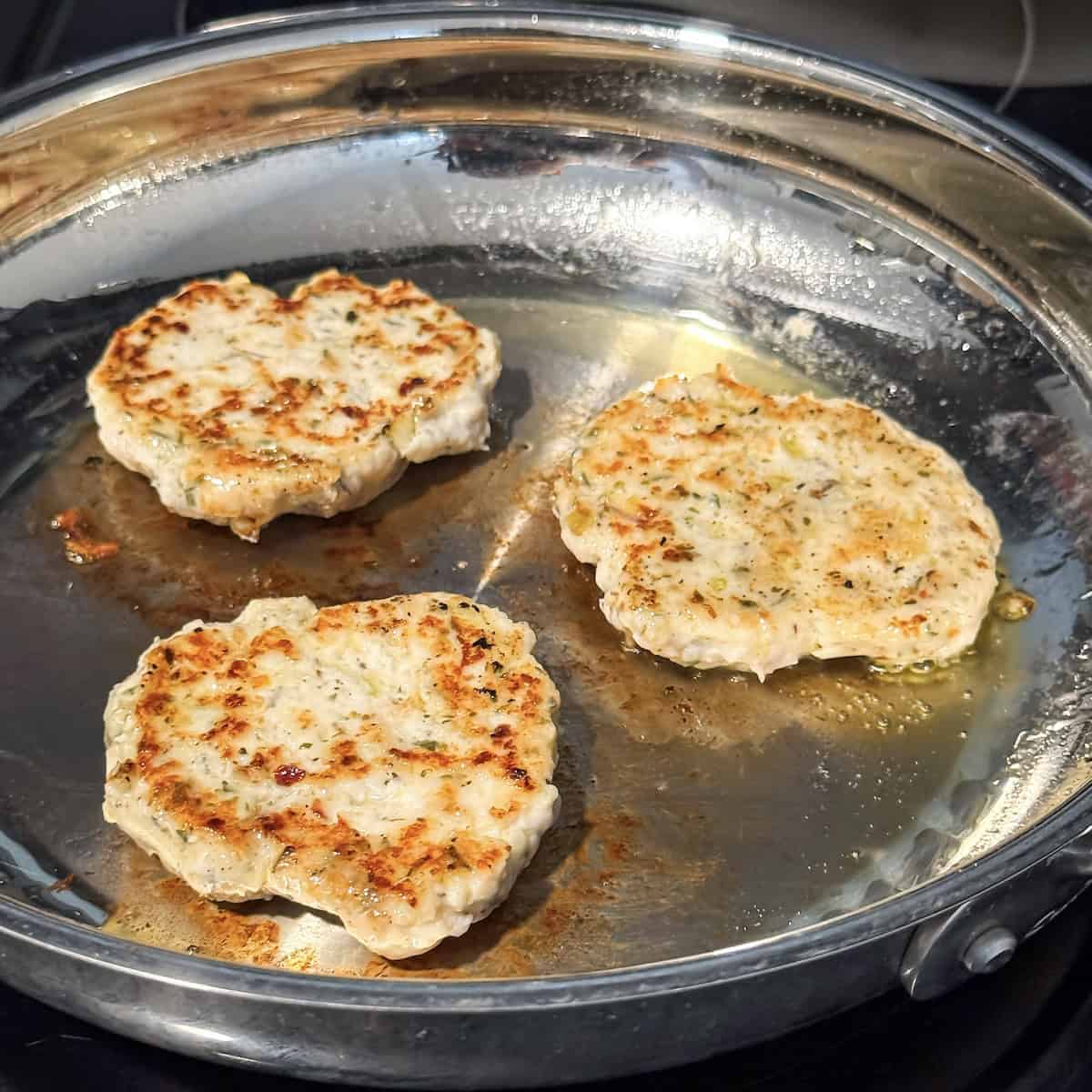 chicken breakfast sausage patties cooking in a skillet.