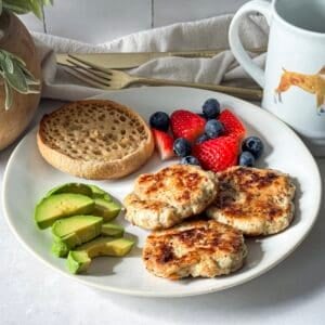 chicken breakfast sausage patties on a plate with avocado, fruit, and half an english muffin side view.