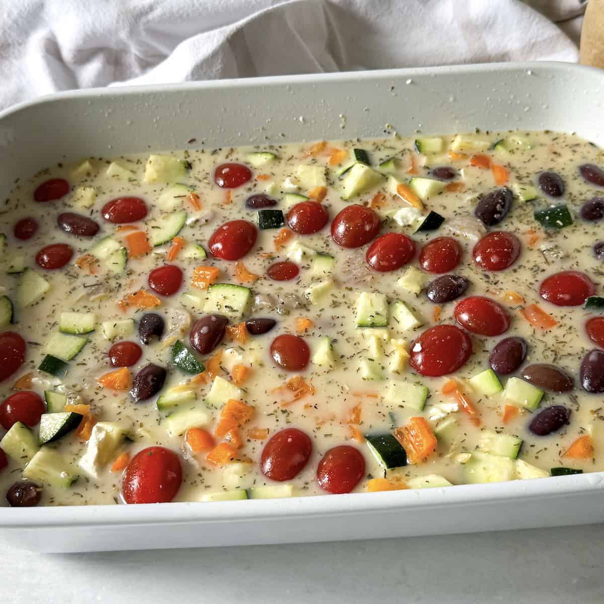 chicken broth added to vegetables and chicken in a baking dish.
