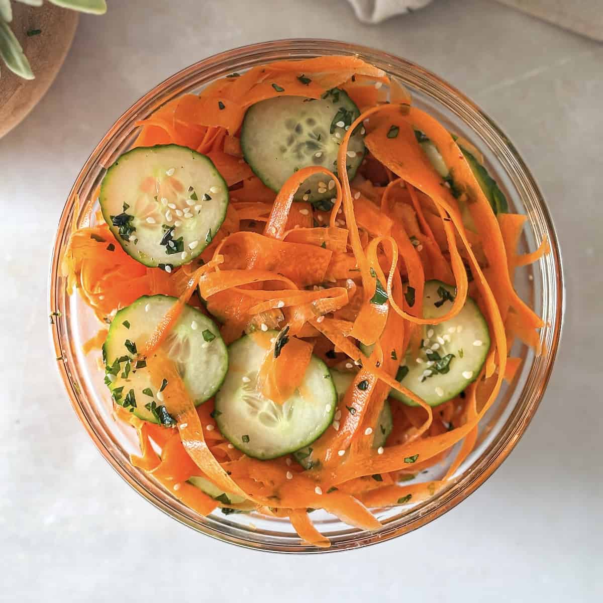 cucumber carrot salad in a glass bowl, overhead view.