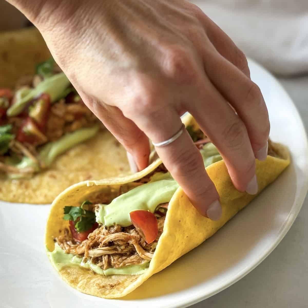 human hand grabbing a chicken taco.