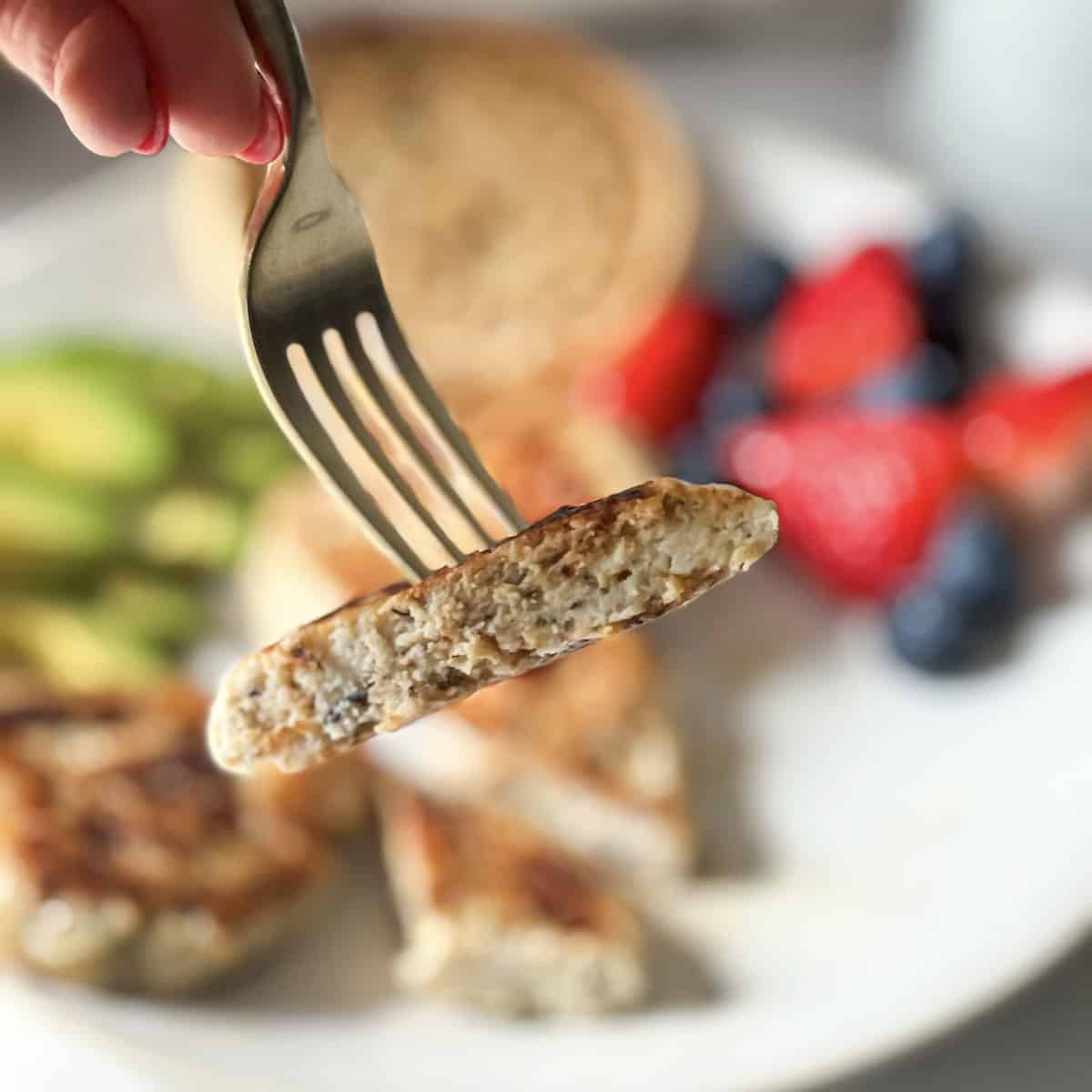 human hand holding a fork with half a chicken breakfast sausage on it.