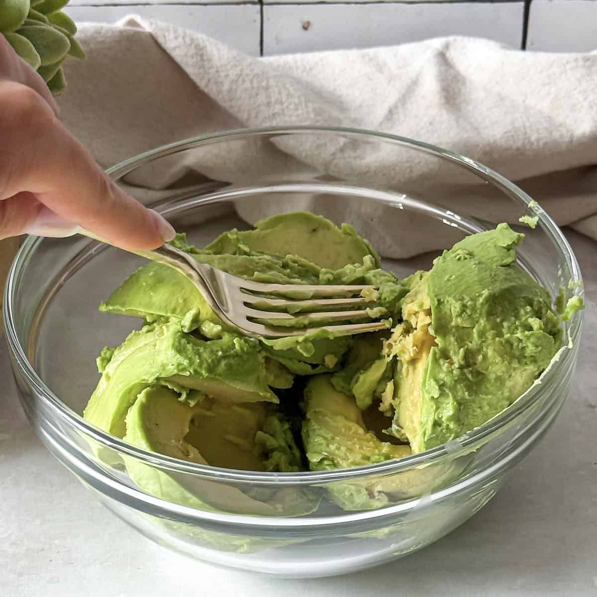 human hand mashing an avocado with a fork.