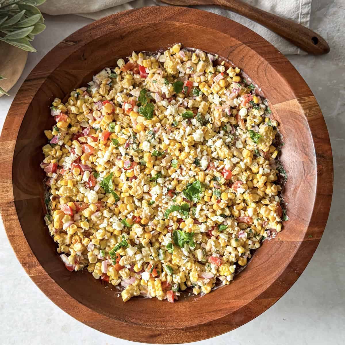 mexican street corn salad mixed in a wooden bowl, overhead view.