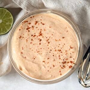 overhead view of dressing for mexican street corn salad in a glass bowl on a table.