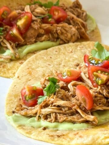 side view of slow cooker chicken tacos with salsa with cherry tomatoes on top.